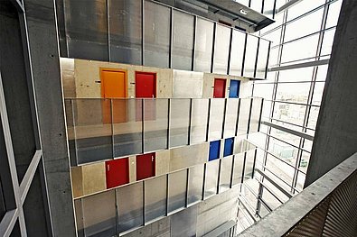 Innenansicht im Studentenwohnheim base 11. Blick im Stiegenhaus auf Stahl-Glas-Verkleidung mit integrierten roten, orangen und blauen quadratischen Elementen, die Glas-Stahl-Wand optisch auflockern.