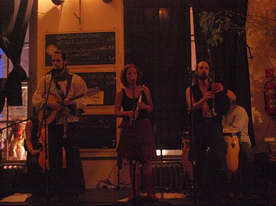 Ein Band, bestehend aus 2 Männern (außen) und einer Frau (Mitte) spielen ihre Instrumente und singen.