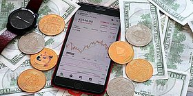 Handy liegt auf Tisch umgeben von Dollarscheinen und KryptoCoins