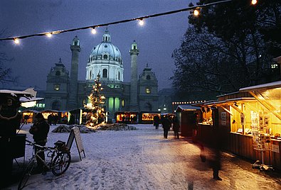 Verschneiter Weihnachtsmarkt vor der beleuchteten Karlskirche.