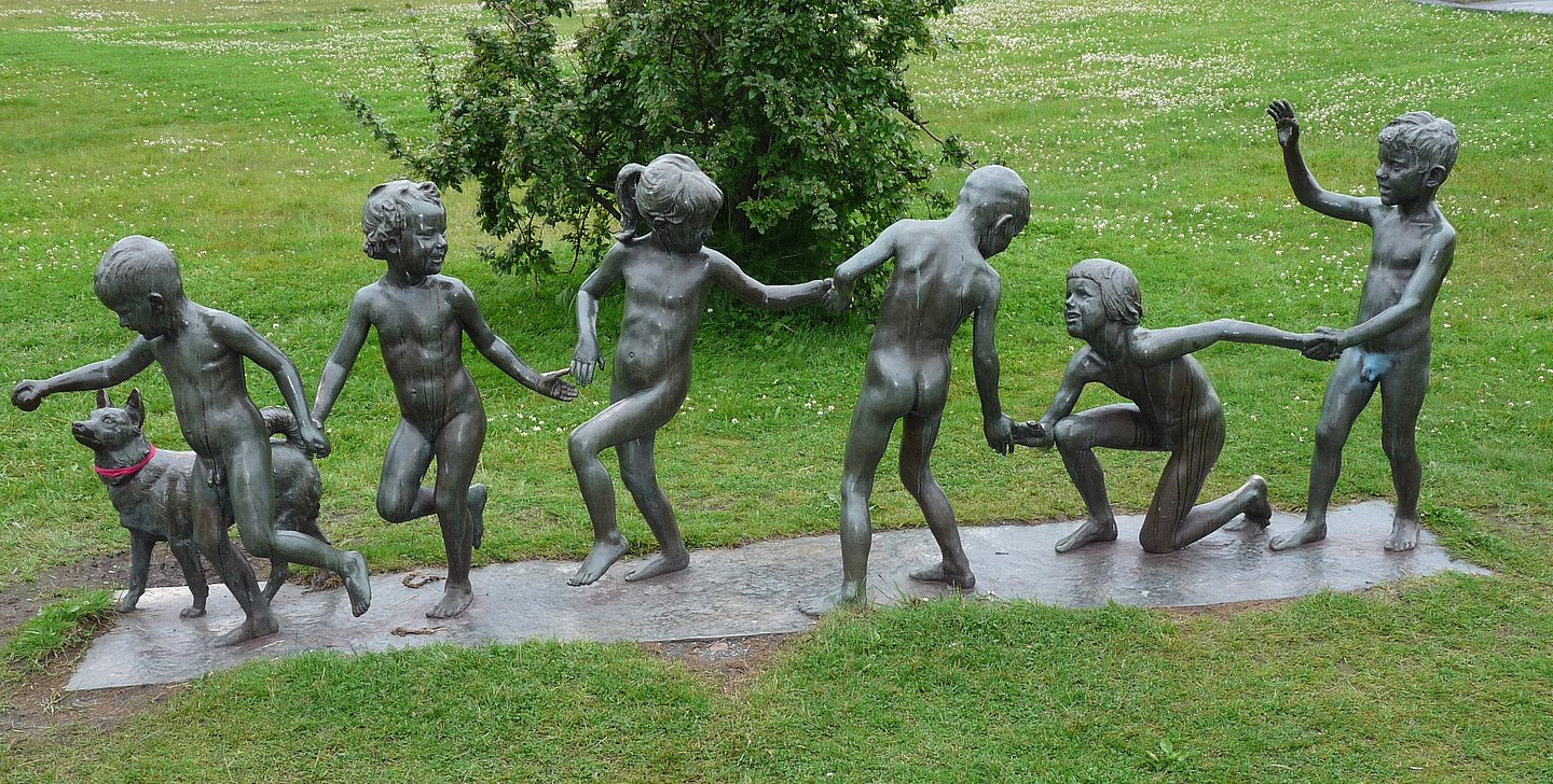 Statuen von spielenden Kindern mit Hund auf einer Wiese