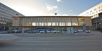 Außenansicht von der Bahnhofshalle des Westbahnhof Wiens, vom Europaplatz aus gesehen. Davor befindet sich eine City Bike Station und eine Bus- sowie Taxihaltestelle.