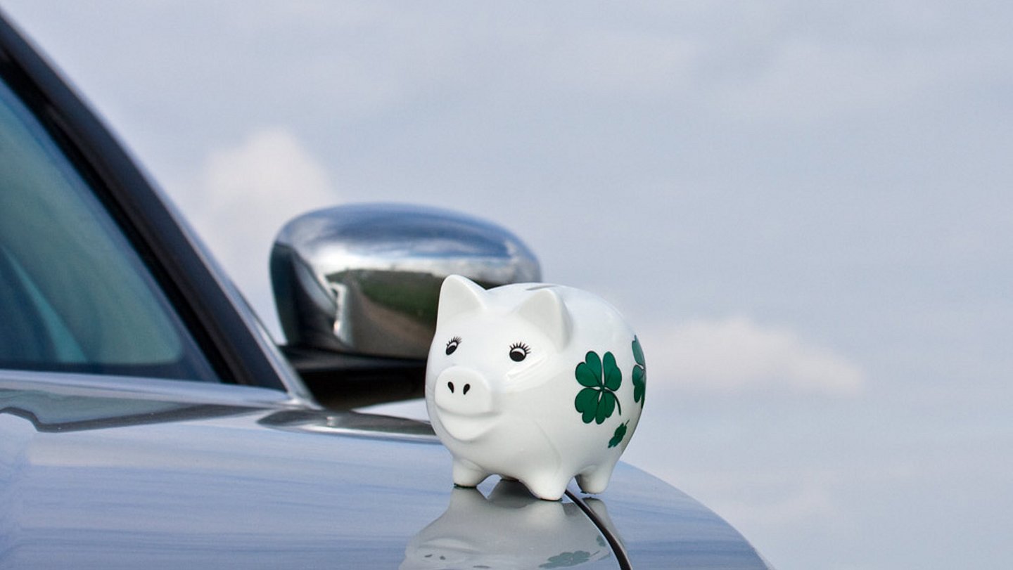 Weißes Sparschein sitzt auf Motorhaube von silberenem Auto.