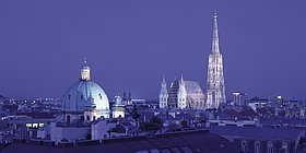 Nachtaufnahme von der beleuchteten Peterskirche und dem Stephansdom.