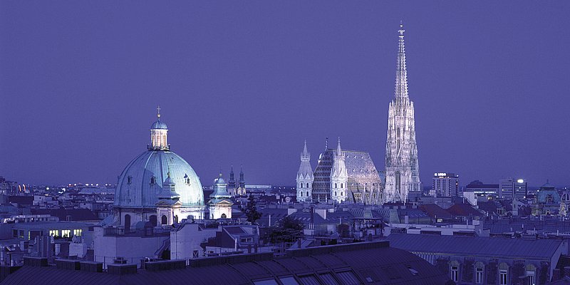 Nachtaufnahme von der beleuchteten Peterskirche und dem Stephansdom.