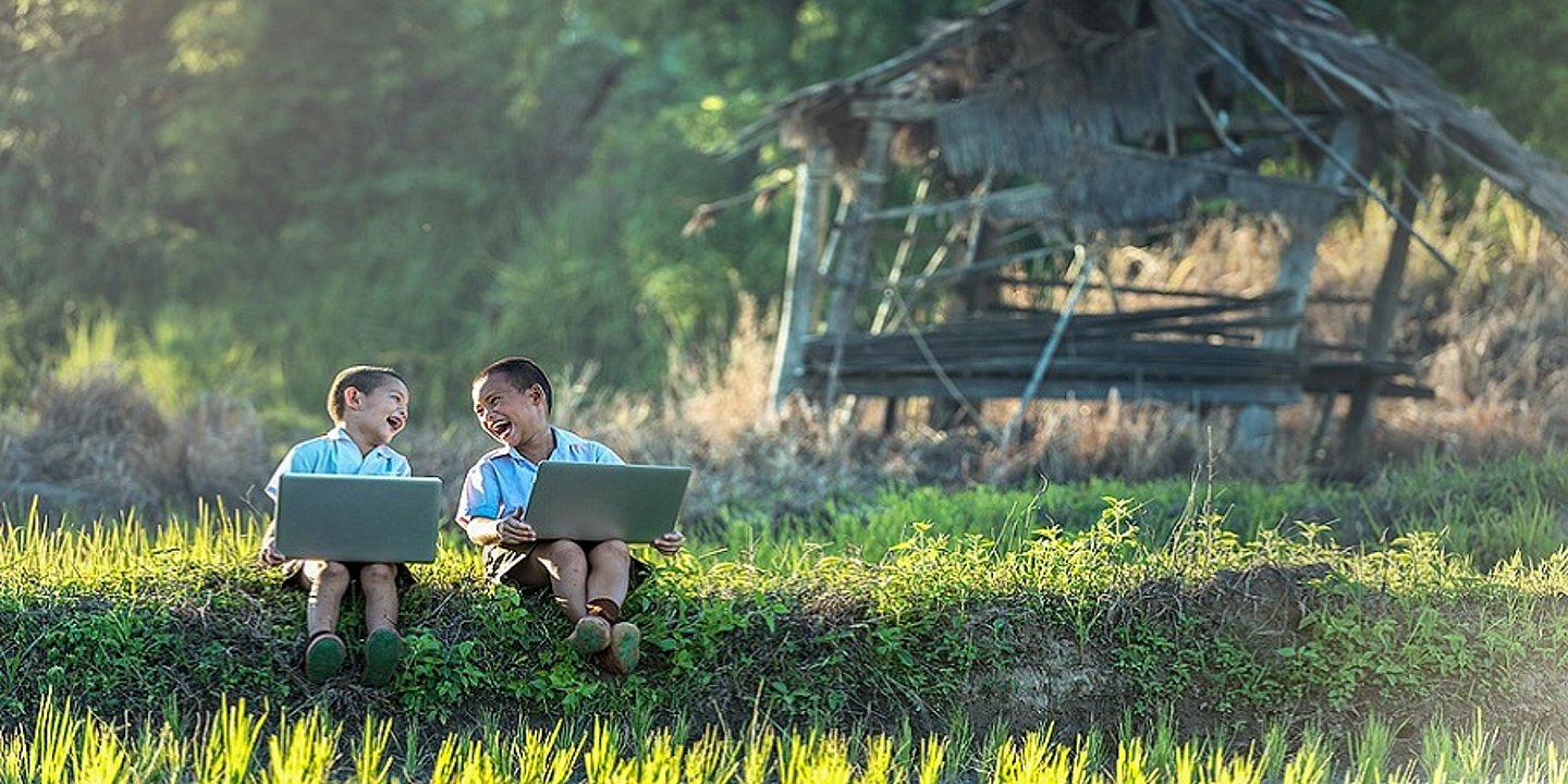 Zwei kleine Buben die mit Laptops in der Natur sitzen