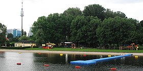 Steg und Strand vom Wasser aus gesehen. Im Hintergrund der Donauturm.