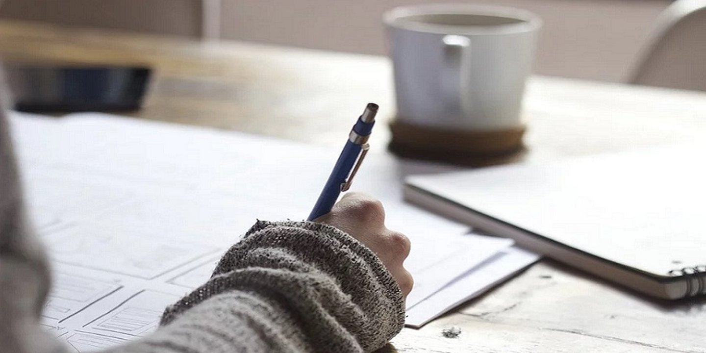 Hand auf Tisch mit Kaffee im Hintergrund beim Lernen