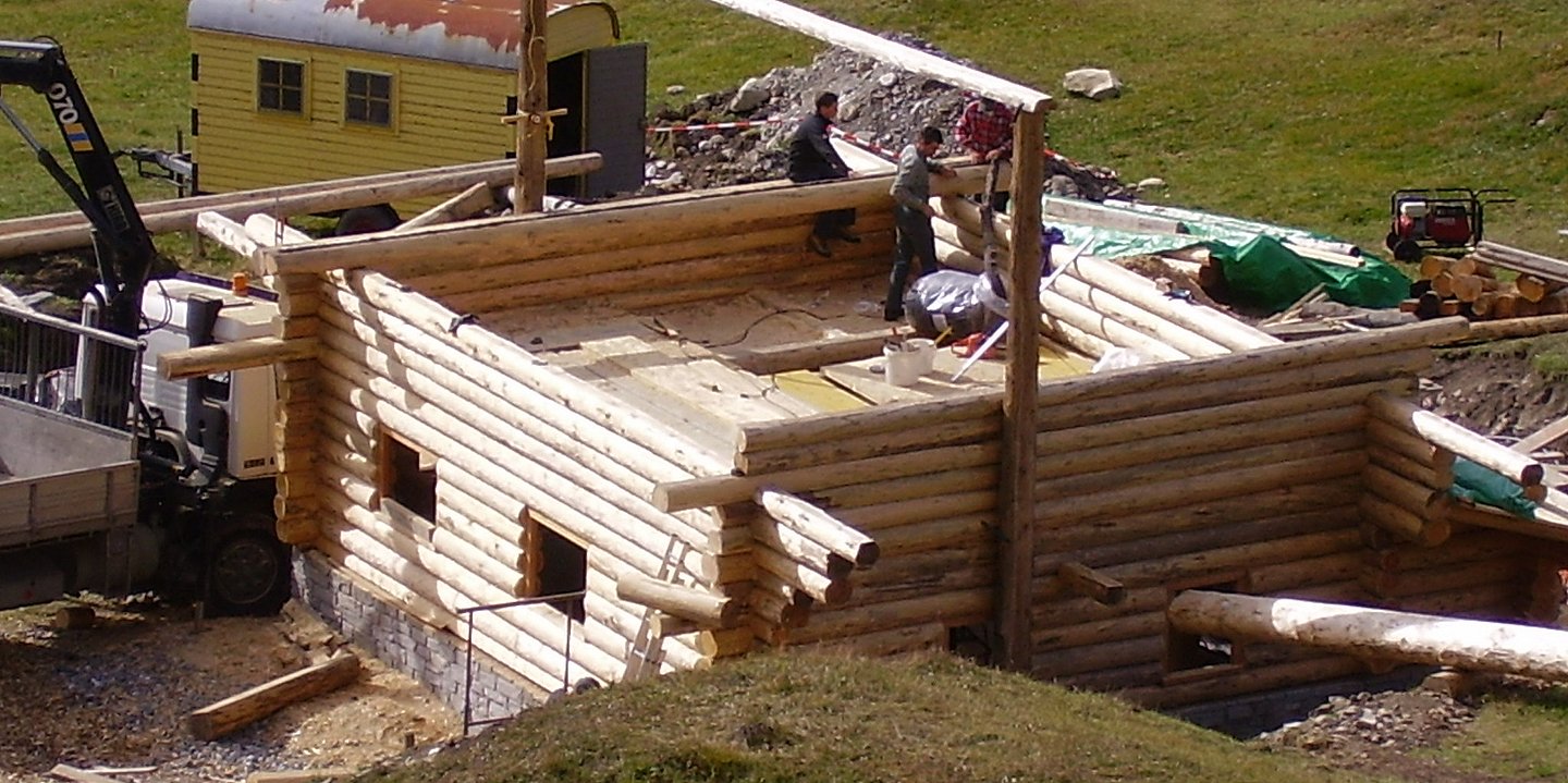 Zwei Arbeiter stehen im ersten Stock eines im Bau befindlichen Blockhauses.