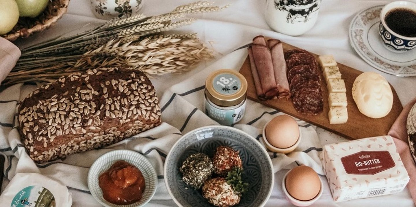 Frühstückstisch von oben gesehen mit Brot, Eier, Butter, Käse, Kuchen und Kaffee