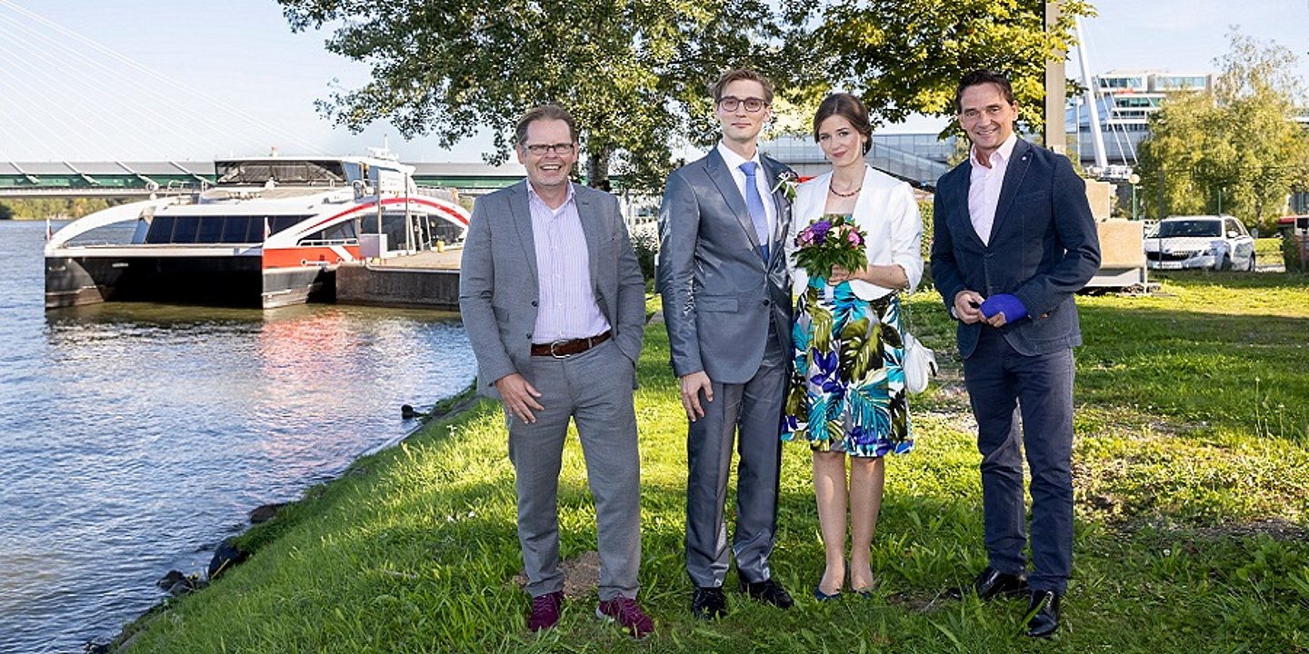 Hochzeitspaar steht im Grünen vor Schiff