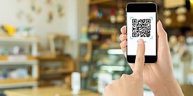 Mensch hält Handy und scannt QR Code in Restaurant