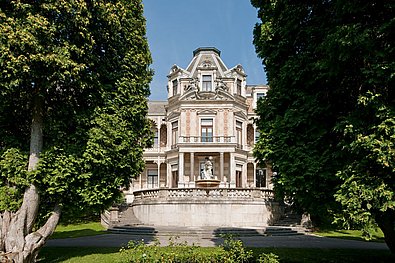 Eine prächtige rosafarbene Villa, davor links und rechts zwei Bäume.