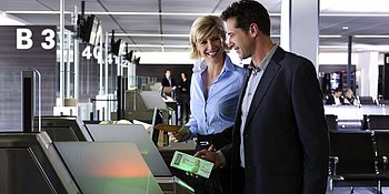 Mann und Frau stehen am Check-In Automaten am Flughafen Wien