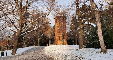 Ein rötlicher Aussichtsturm erhebt sich schneebedeckt von einem Hügel in einem Park