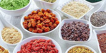 Verschiedene Superfoods wie Datteln und Chiasamen in kleinen Porzelanschüsseln