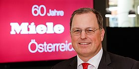 Miele Österreich GF Martin Melzer vor einem Screen mit Schriftzug "60 Jahre Miele Österreich"