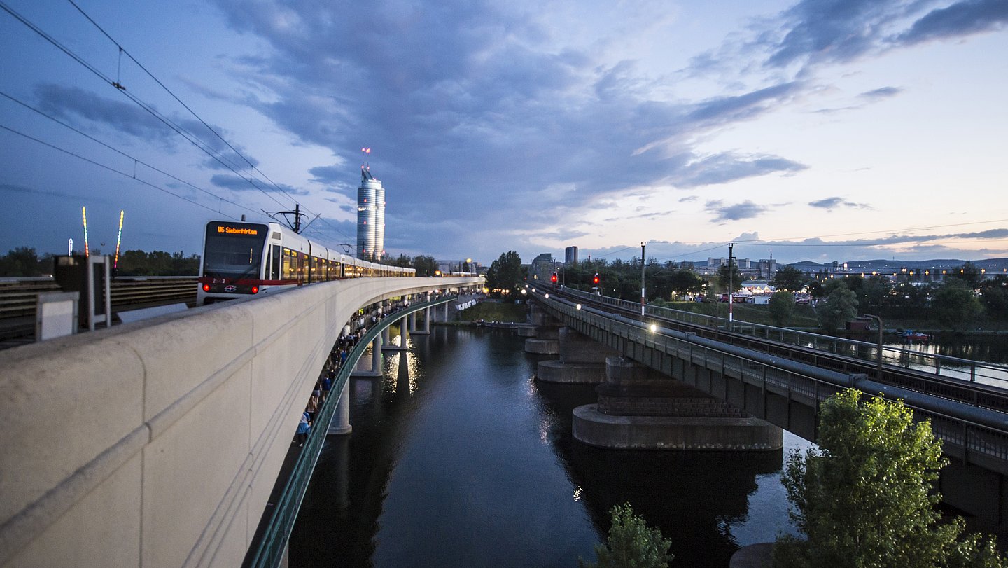 U-Bahn überquert in der Dämmerung eine Brücke über die Donau