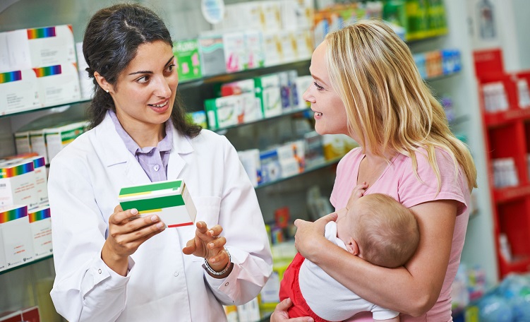 Apothekerin berät eine Frau mit Baby im Arm.